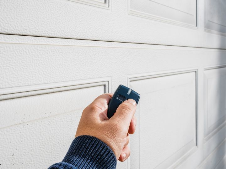 Hand holding a garage door opener toward a white paneled garage door