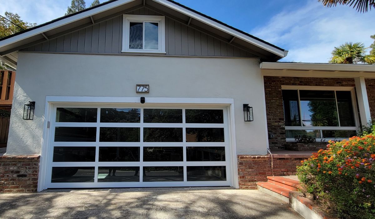 Single-story house with white garage door, front porch, and landscaped entryway under a blue sky