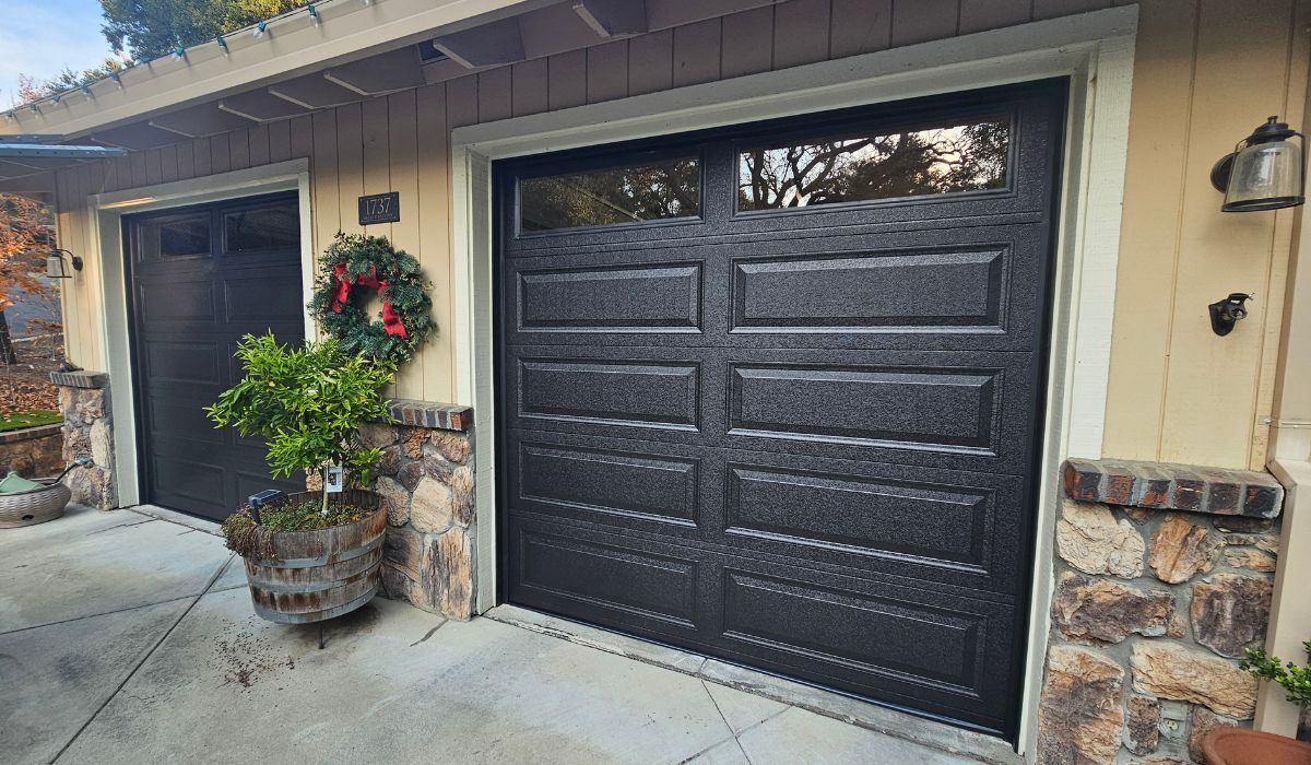 Front of a house with black garage doors, stone accents, and a potted plant by the entryway