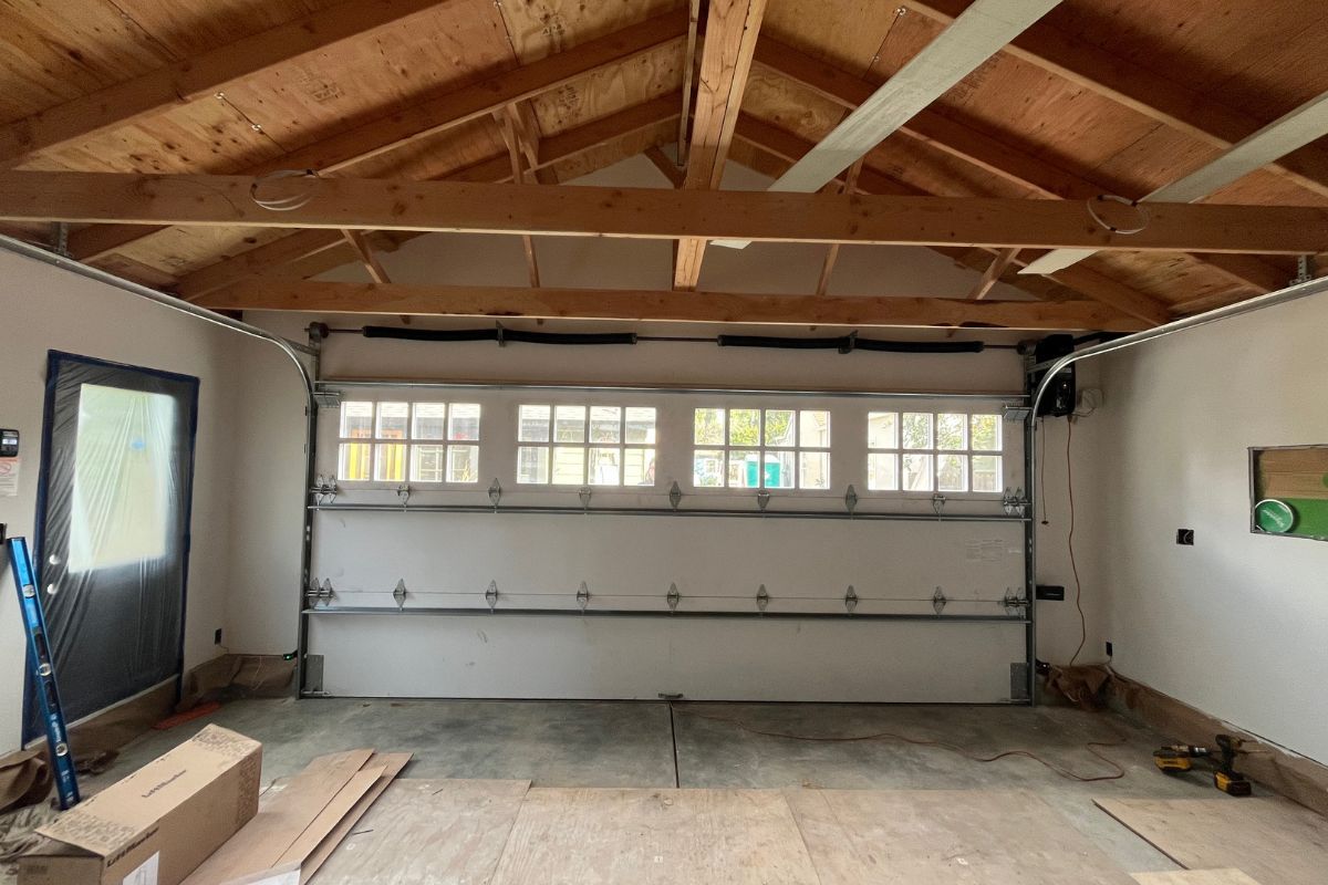 Empty garage interior with exposed wooden rafters, white walls, and a small row of windows.