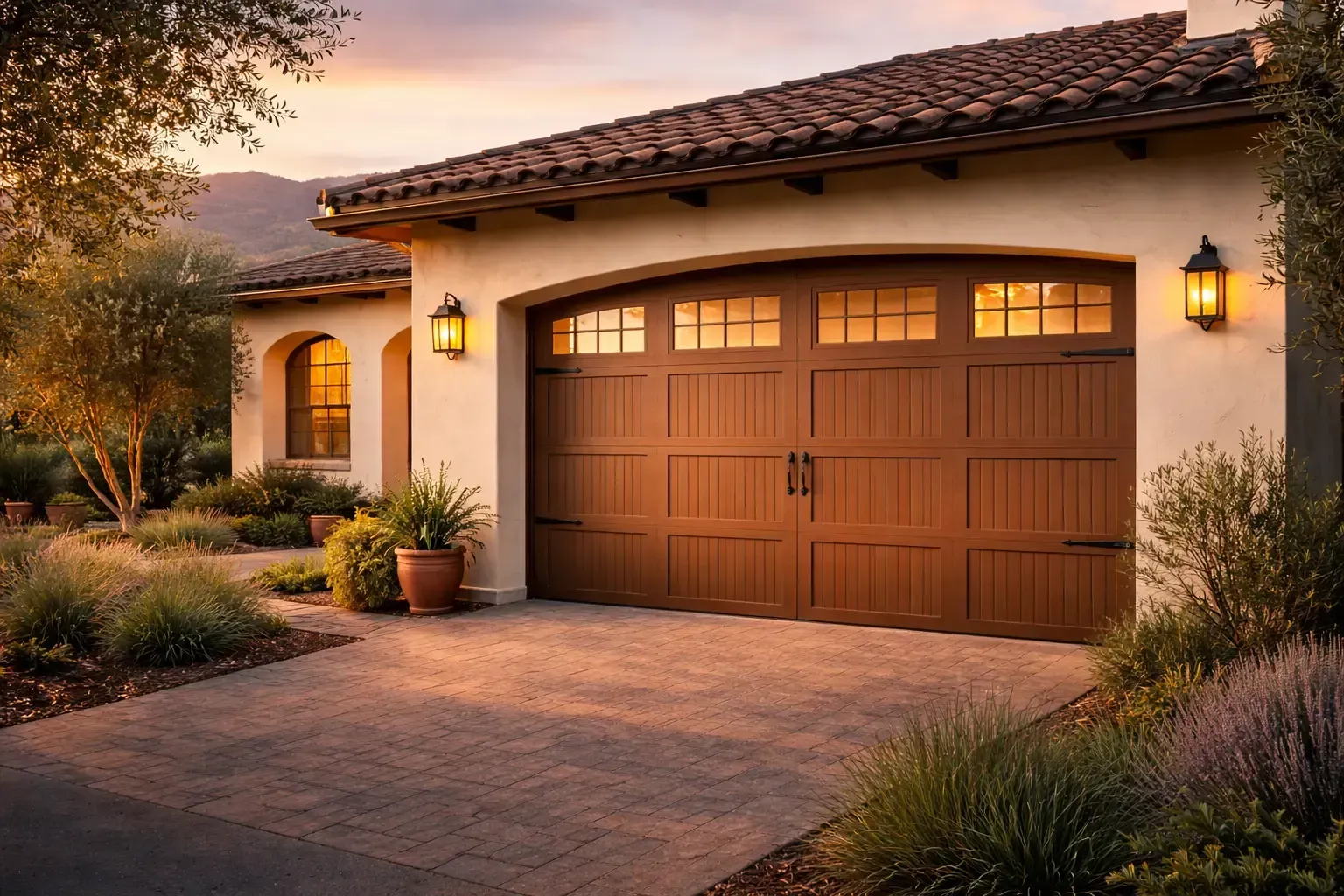 Warmly lit stucco house with a wooden garage door and desert landscaping at dusk