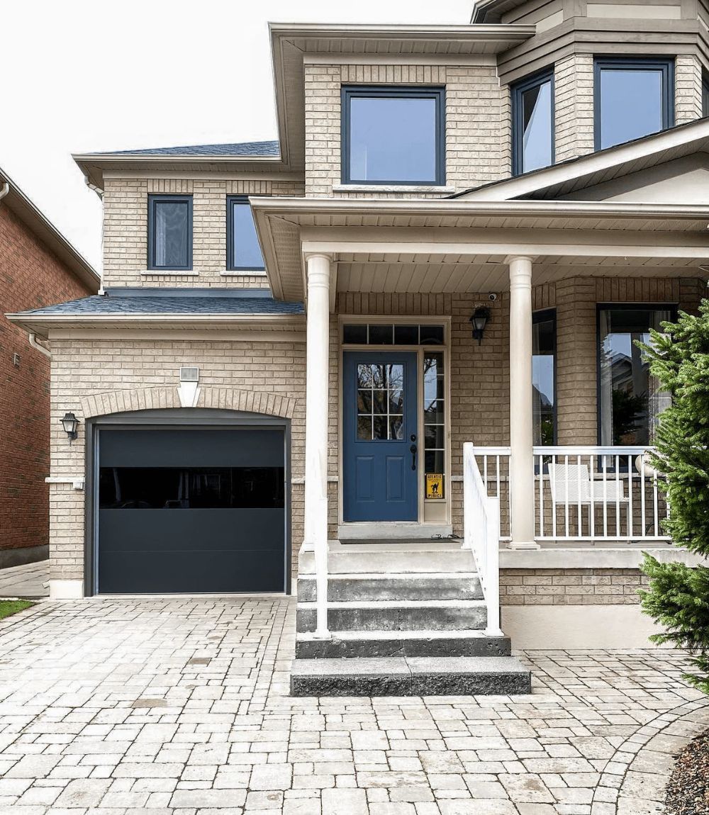 Two-story beige brick house with blue front door, black garage, and stone driveway