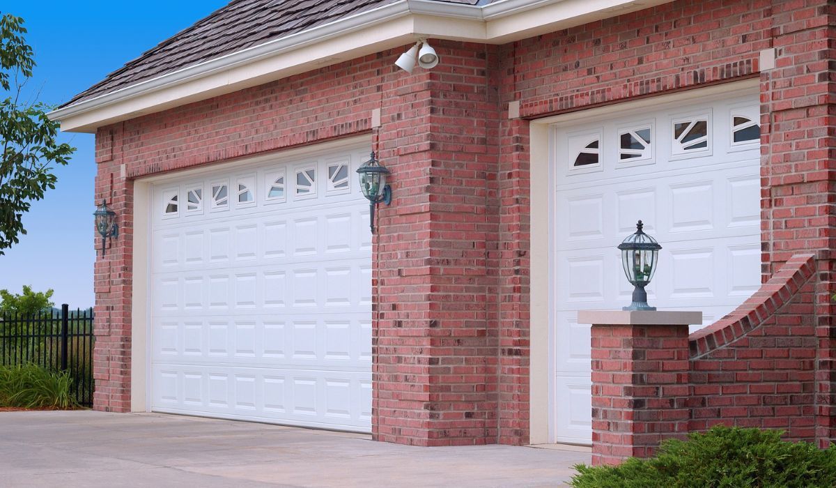 Brick house exterior with two white garage doors and a front lamp by the driveway
