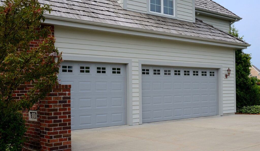 Two-car gray garage doors on a white house with brick trim and a driveway