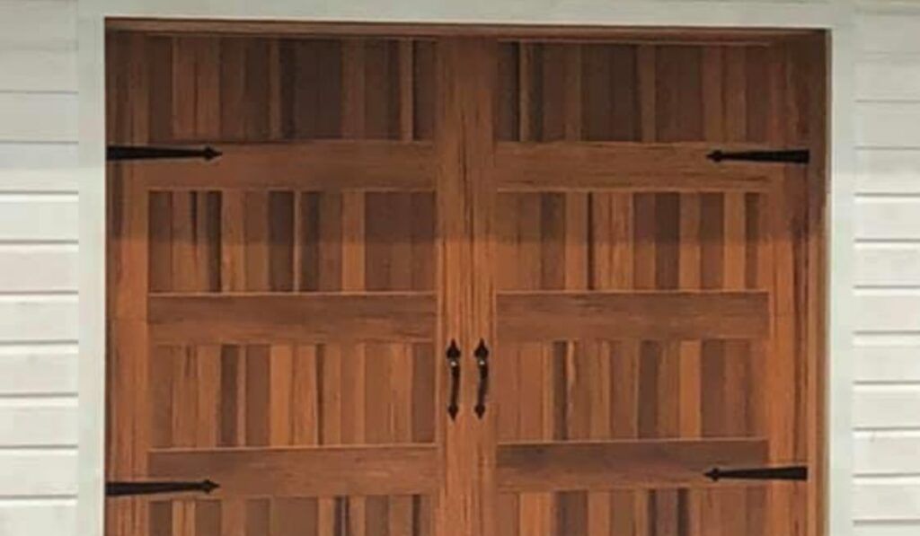 Wooden double garage doors with black handles set in a white-sided exterior wall.