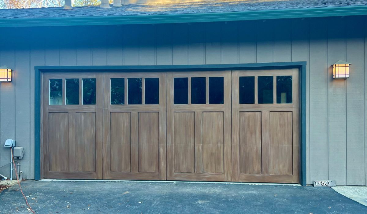Three-car wooden garage door with teal trim on a gray house exterior