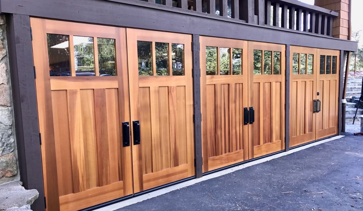 Wooden garage-style doors with window panels on a building exterior, beside a driveway