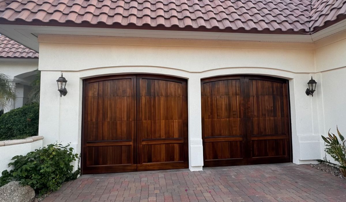 Two wooden garage doors on a white stucco house with a brick driveway and tile roof