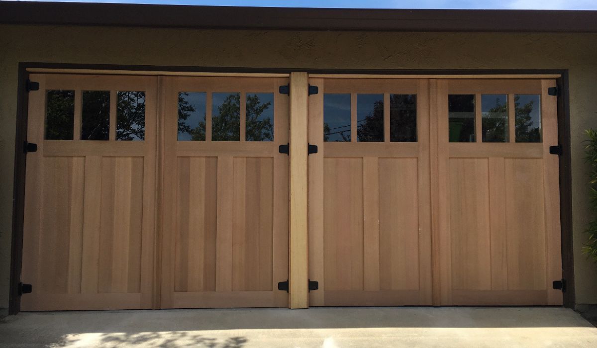 Wooden double garage doors with small windows in a beige exterior wall