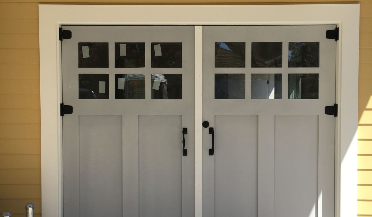 White double garage doors with small windows on a beige house exterior