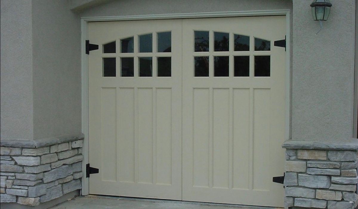 Beige garage door with small windows set in a stucco wall with stone trim