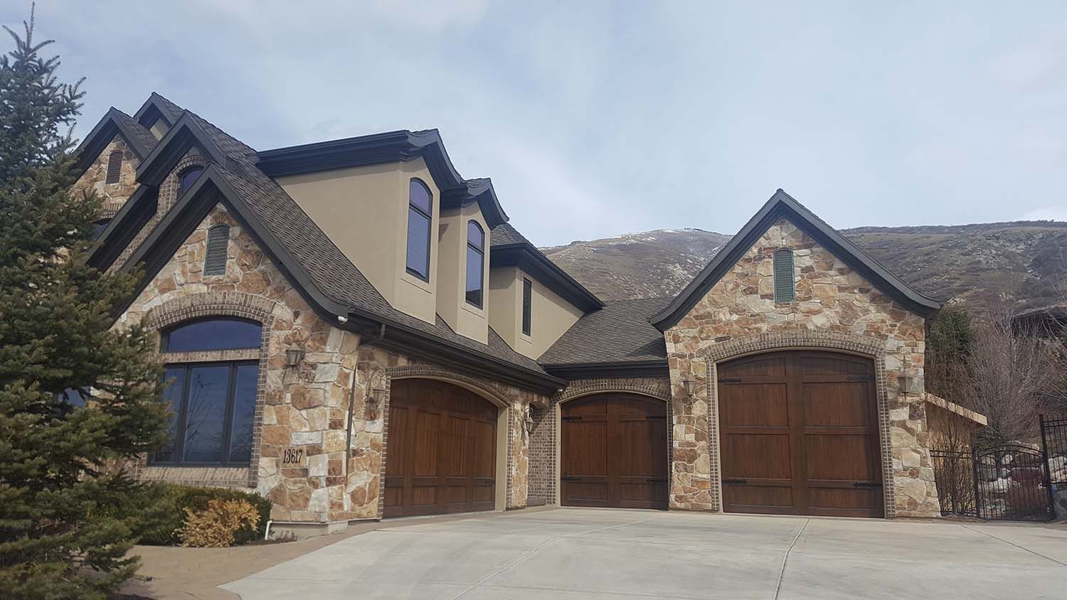 Stone and stucco suburban house with three wooden garage doors and a peaked roof