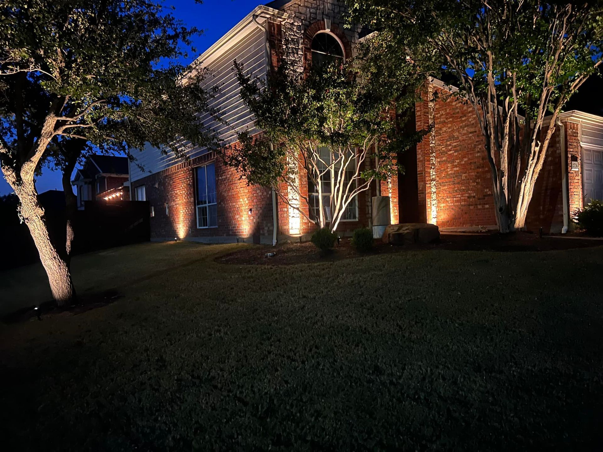 A house is lit up at night with trees in front of it