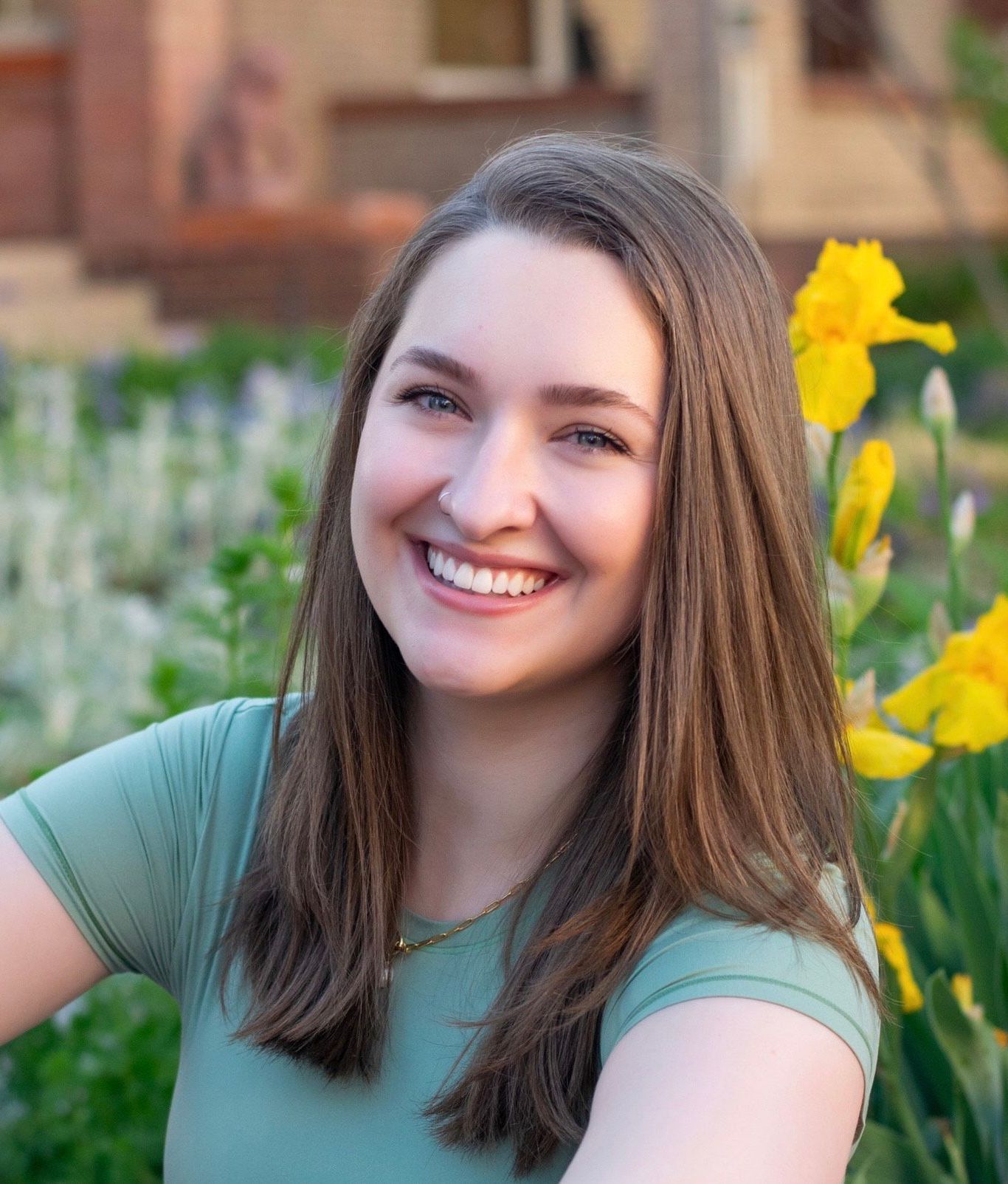 A woman wearing a green shirt and a white sweater is smiling for the camera.