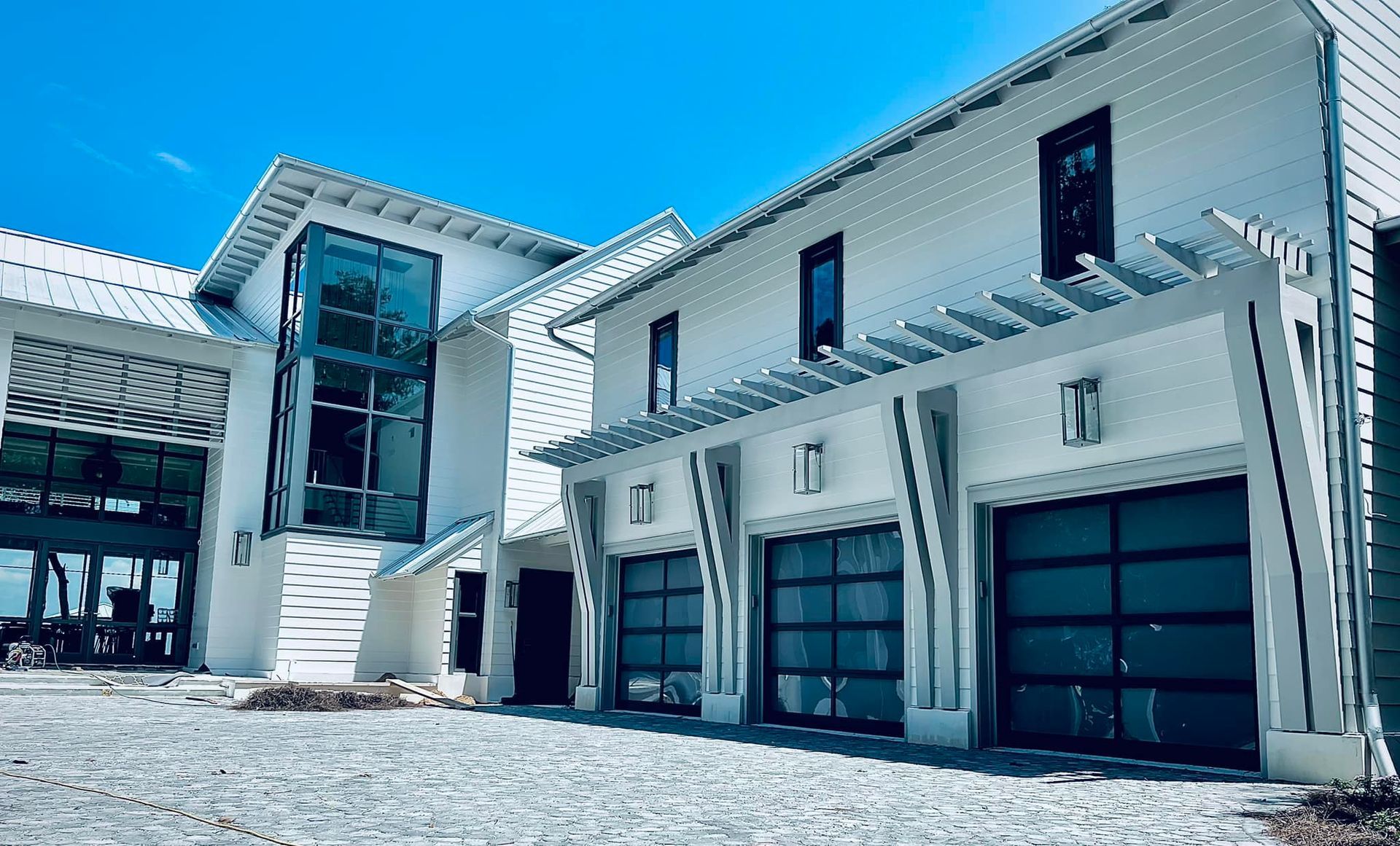 Modern white house exterior with large windows and a glass entryway under a bright blue sky