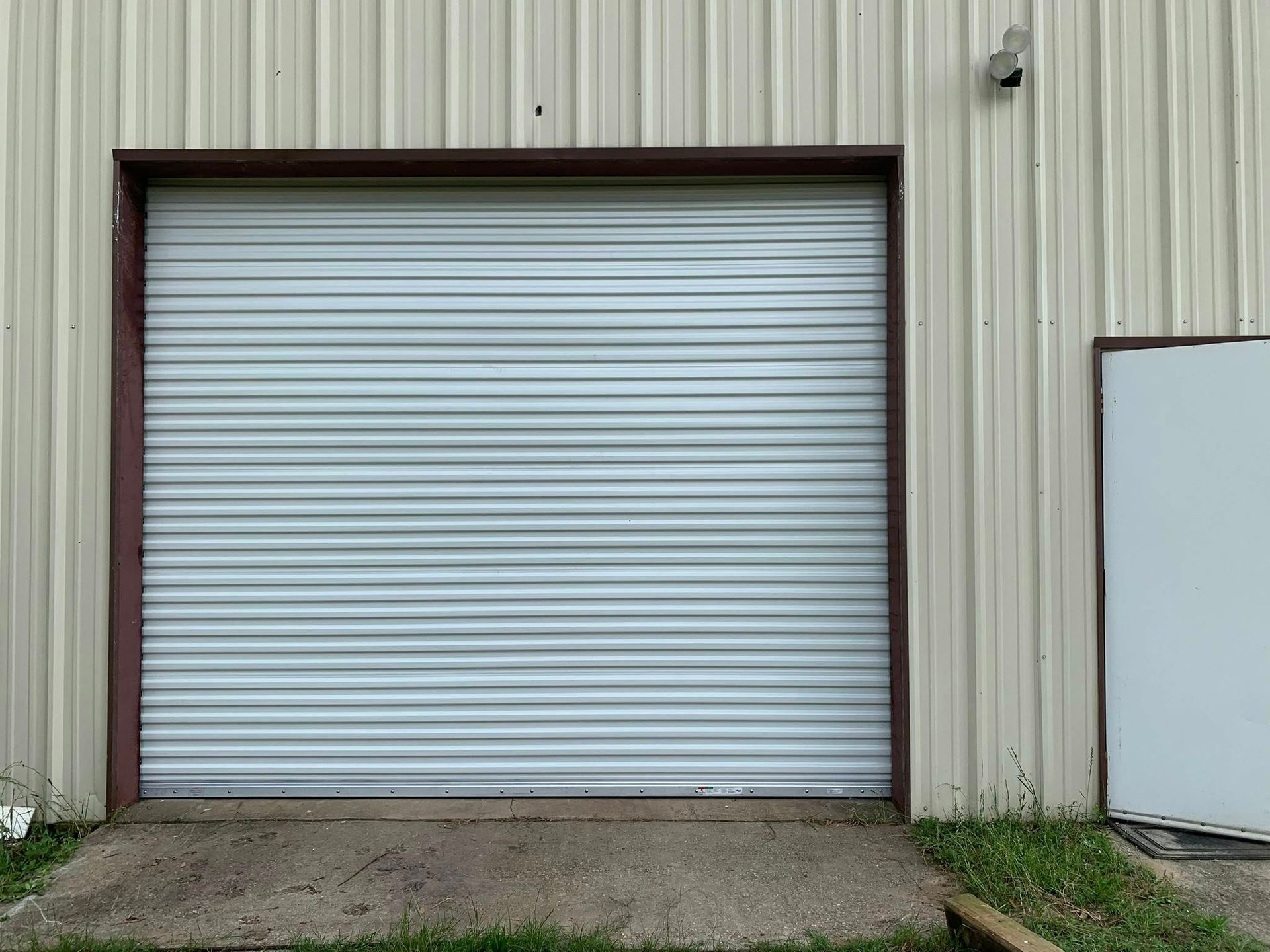 Closed white roll-up garage door on a beige metal building, with a small white side door visible.