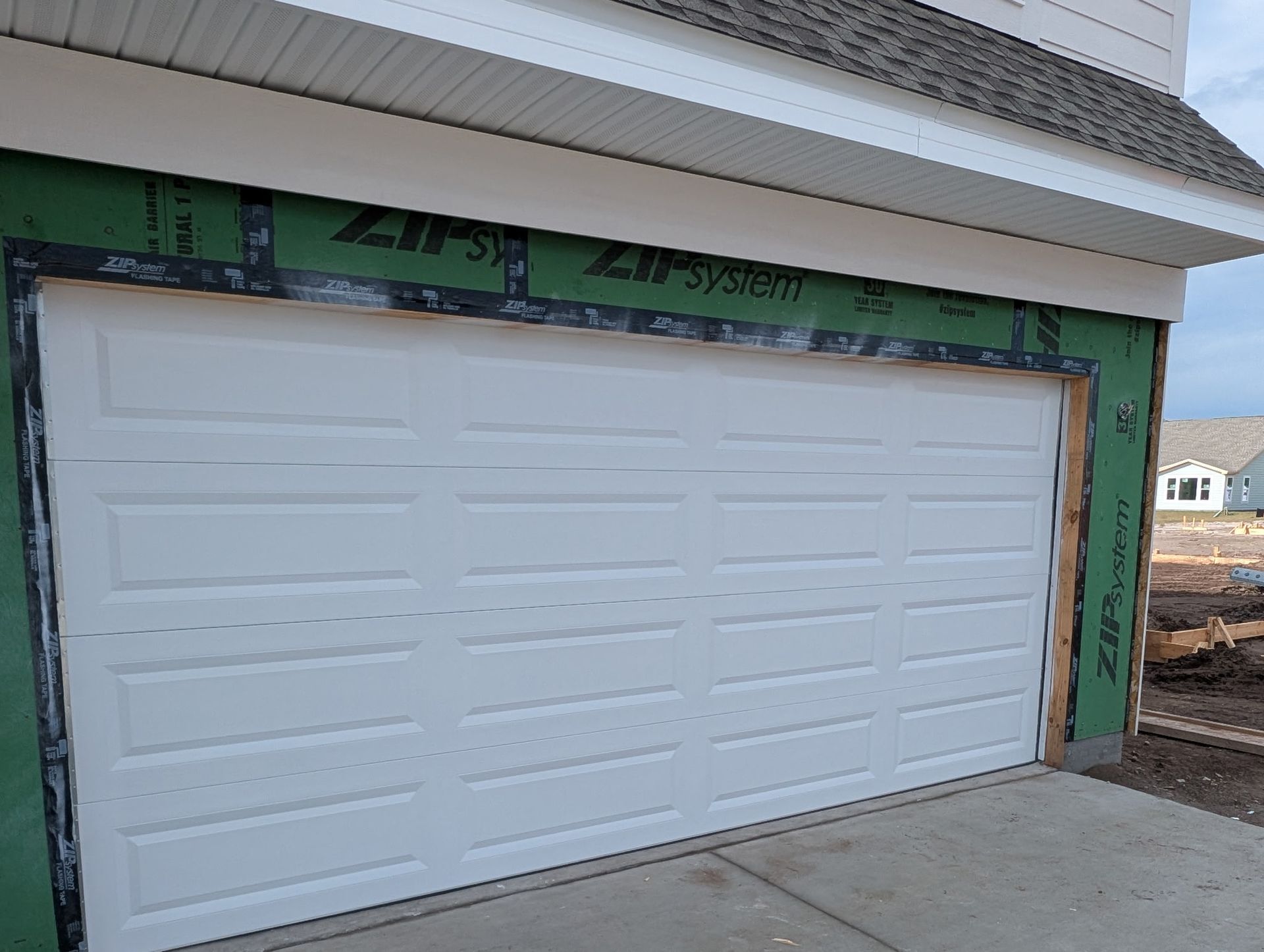 White garage door on a house under construction, with green trim and exposed framing above the opening