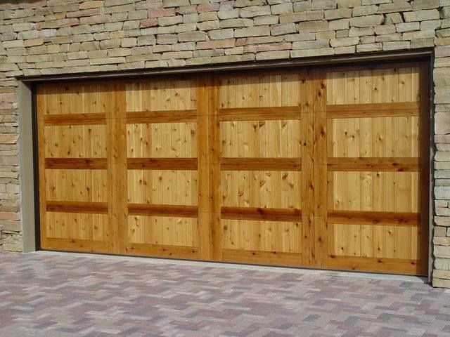 Wooden double garage door set in a stone wall with a brick-paved driveway in front
