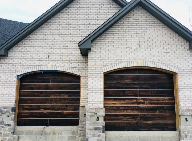 Two dark wooden garage doors in a light brick house facade