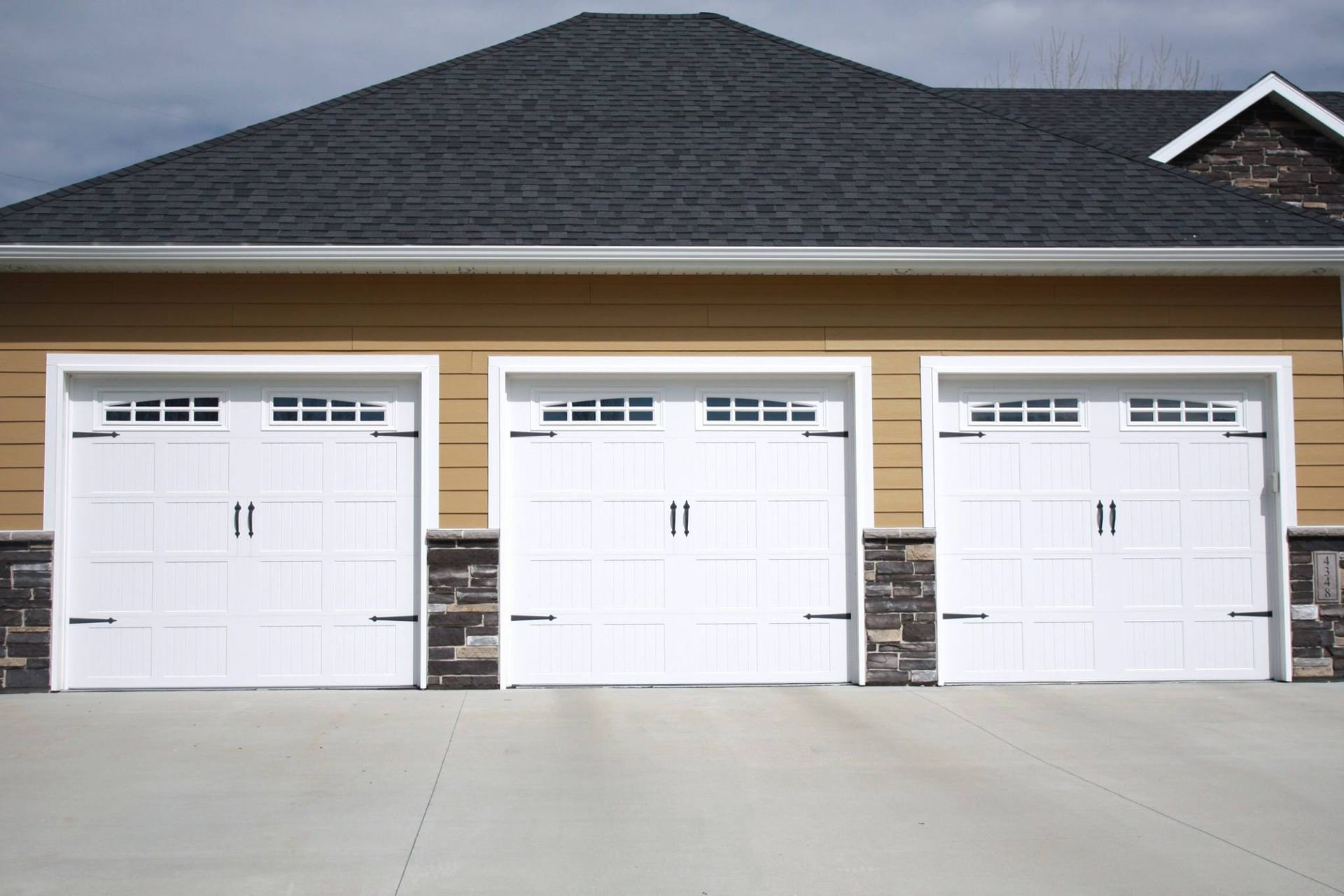 Three white garage doors on a beige house with a dark shingled roof.