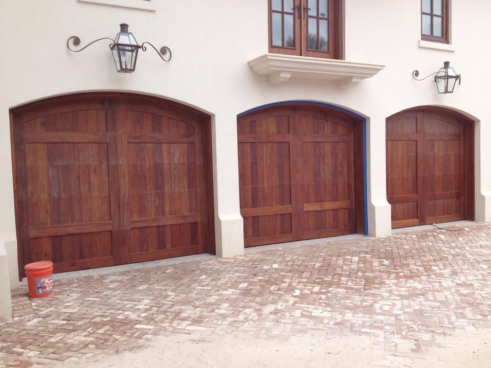 Three wooden garage doors on a white stucco house with cobblestone driveway and wall lanterns
