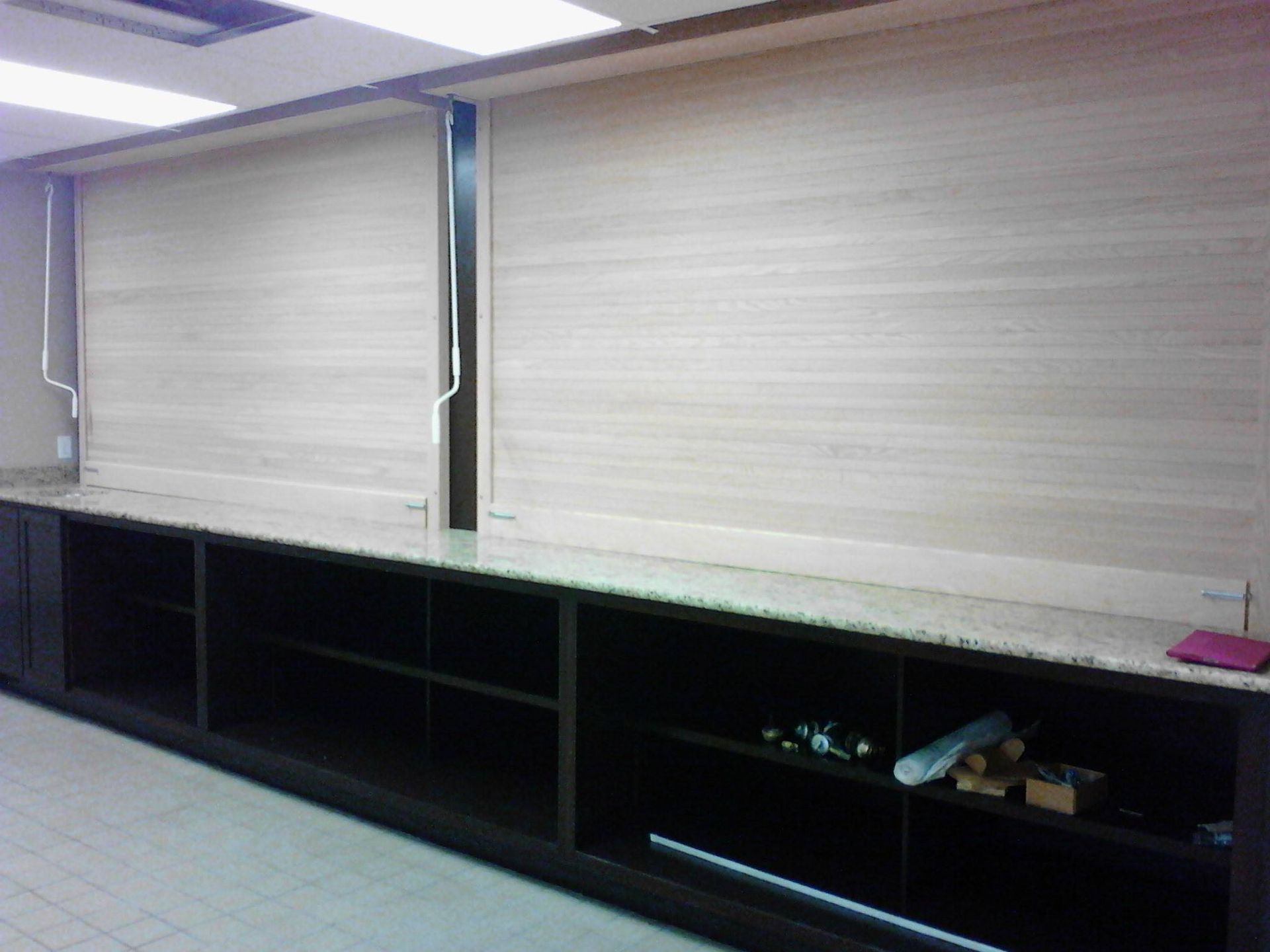 Closed window blinds above a long black shelf in an office or classroom