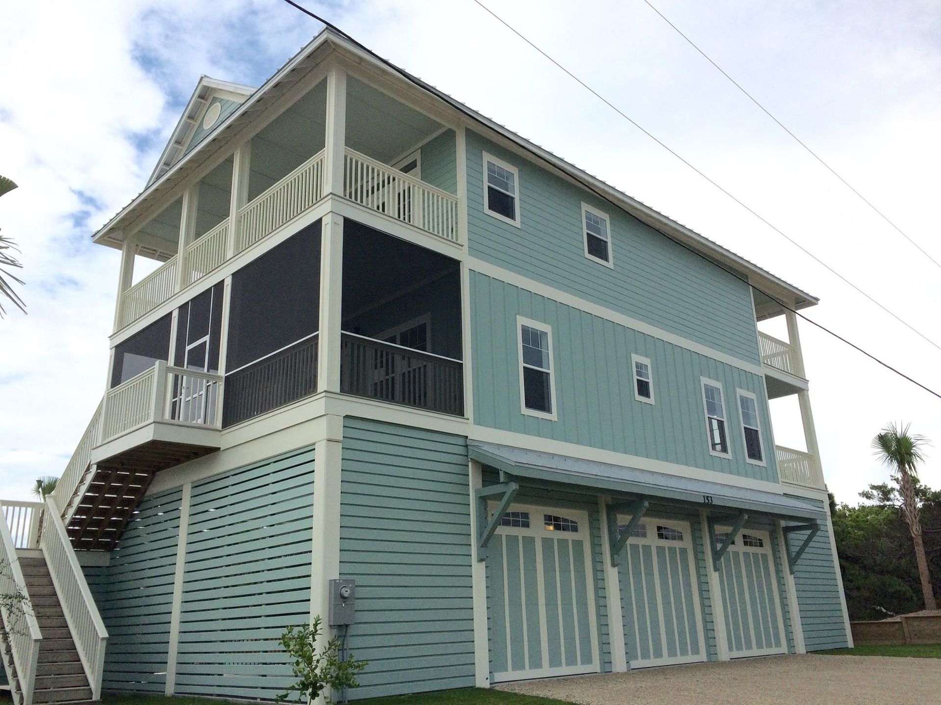 Two-story light blue beach house with balconies and ground-level garage