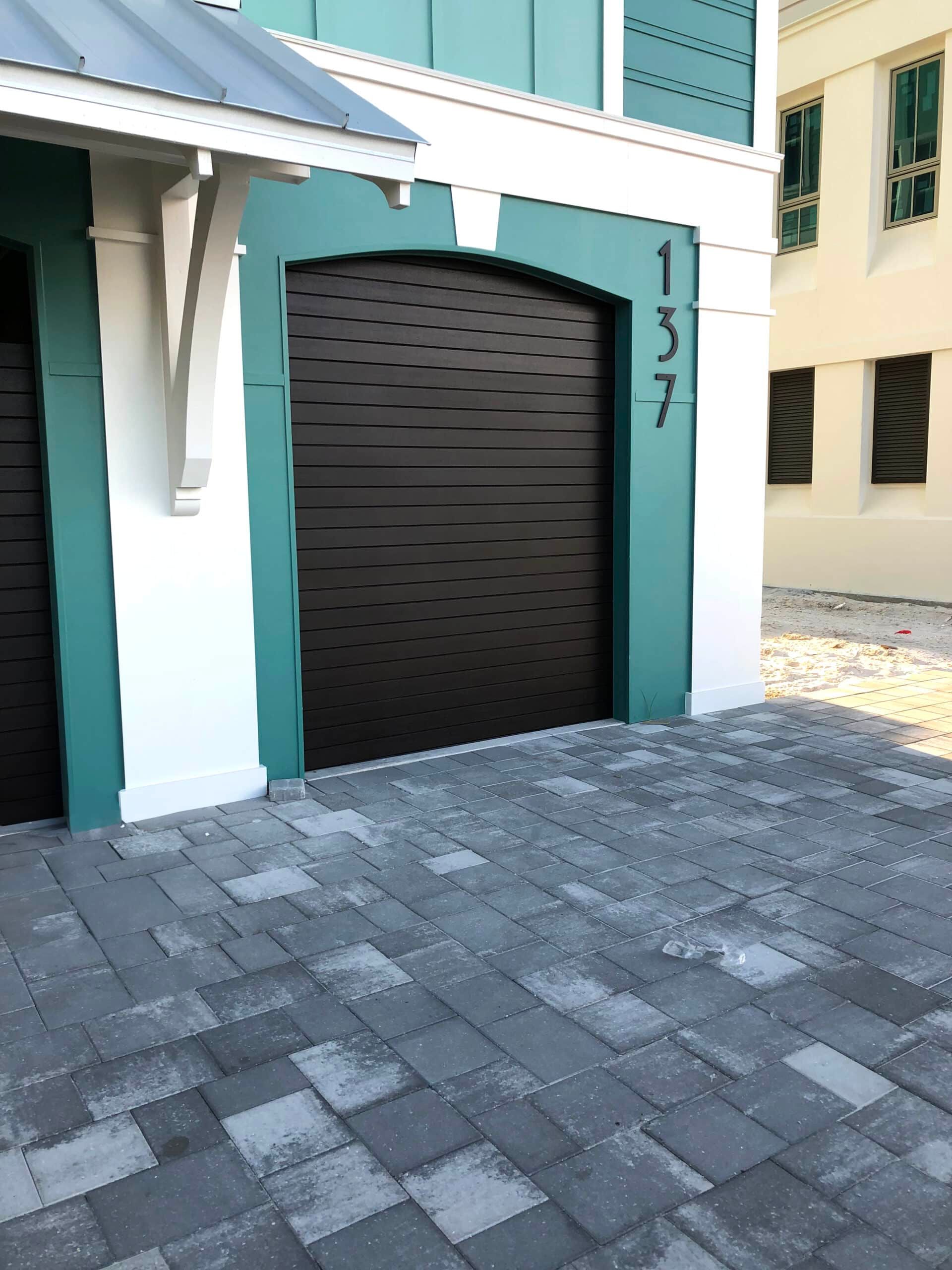 Mint and white building entrance with black garage door and cobblestone pavement