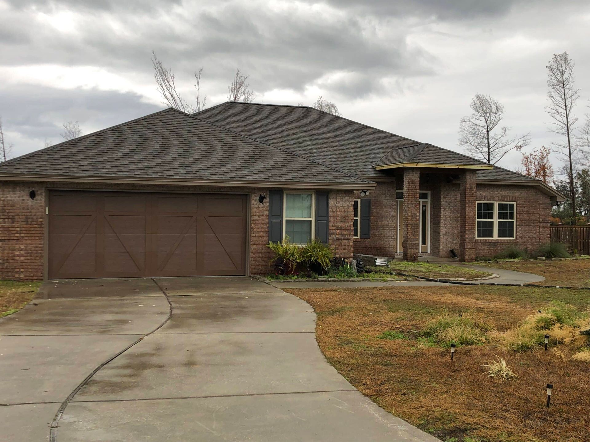 Single-story brick house with a two-car garage and wet driveway on a cloudy day