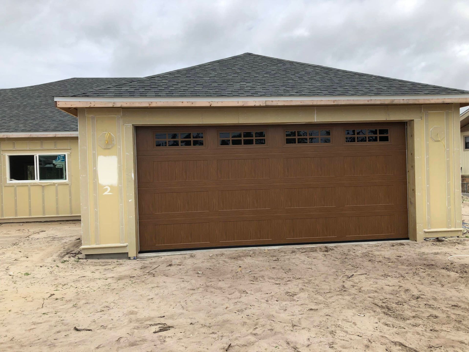 Front view of a tan house with a brown garage door and dark shingled roof