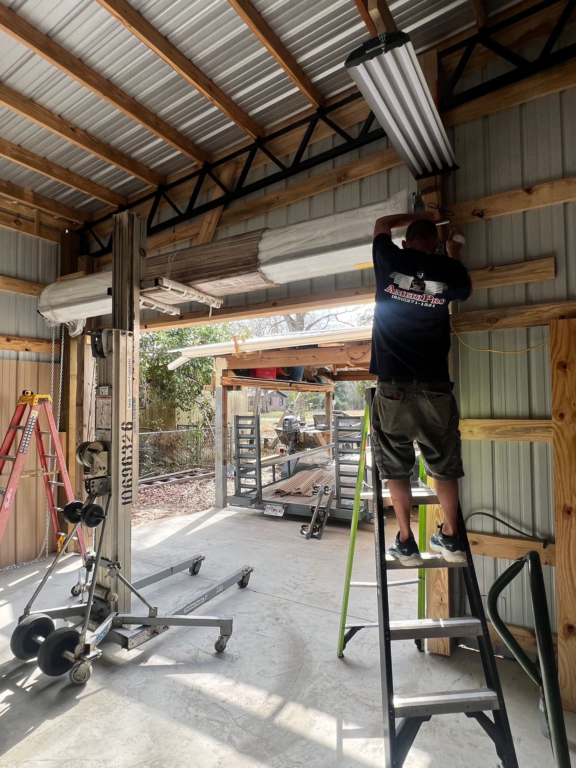 Two workers in blue overalls installing ceiling trim in a room with wood planks.