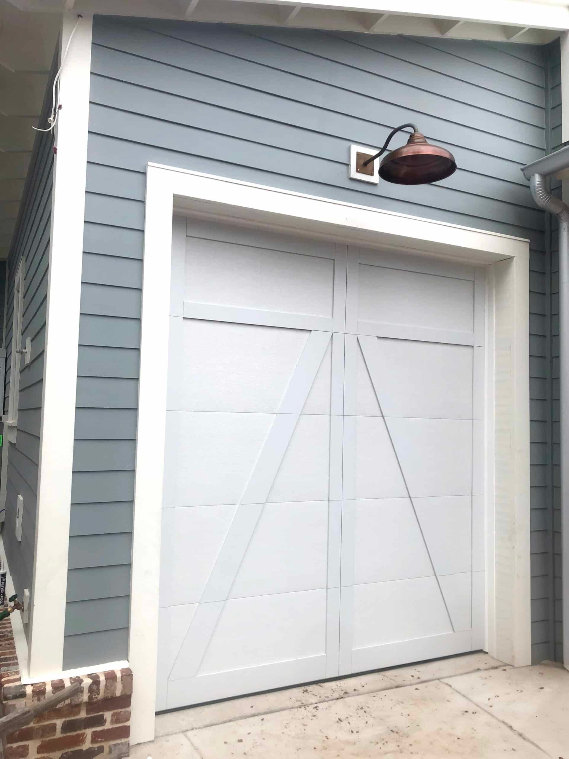 White garage door on a gray house exterior with a small wall-mounted light above it.