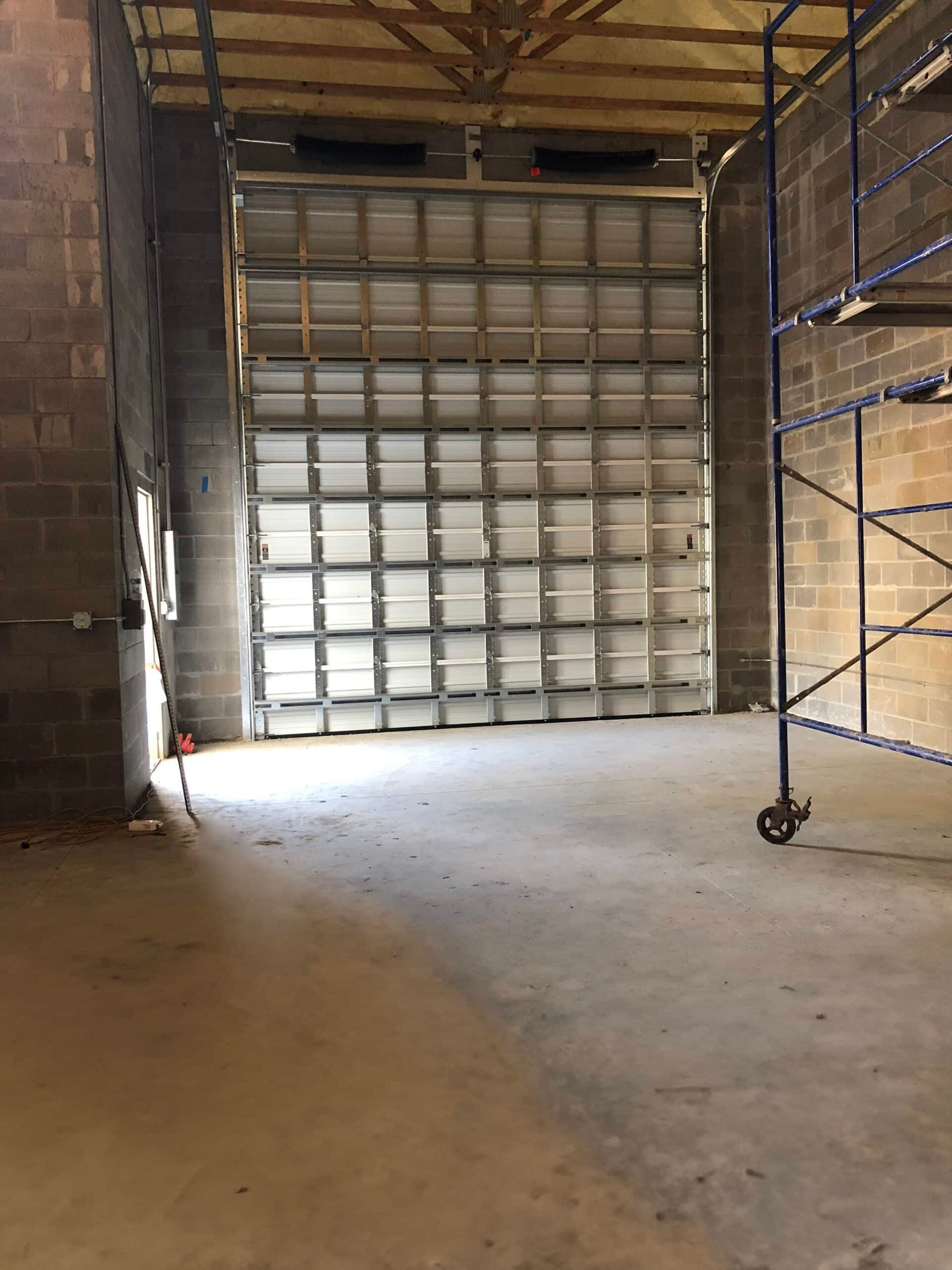 Empty warehouse interior with a concrete floor, metal shelving, and a large roll-up door.