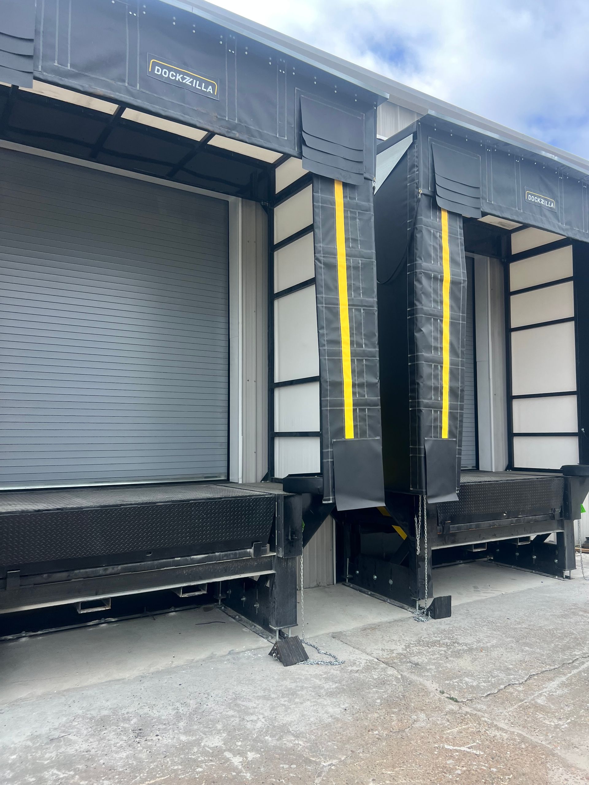 Warehouse loading docks with two truck bays, one closed gray door and one open dock with yellow safety strips.