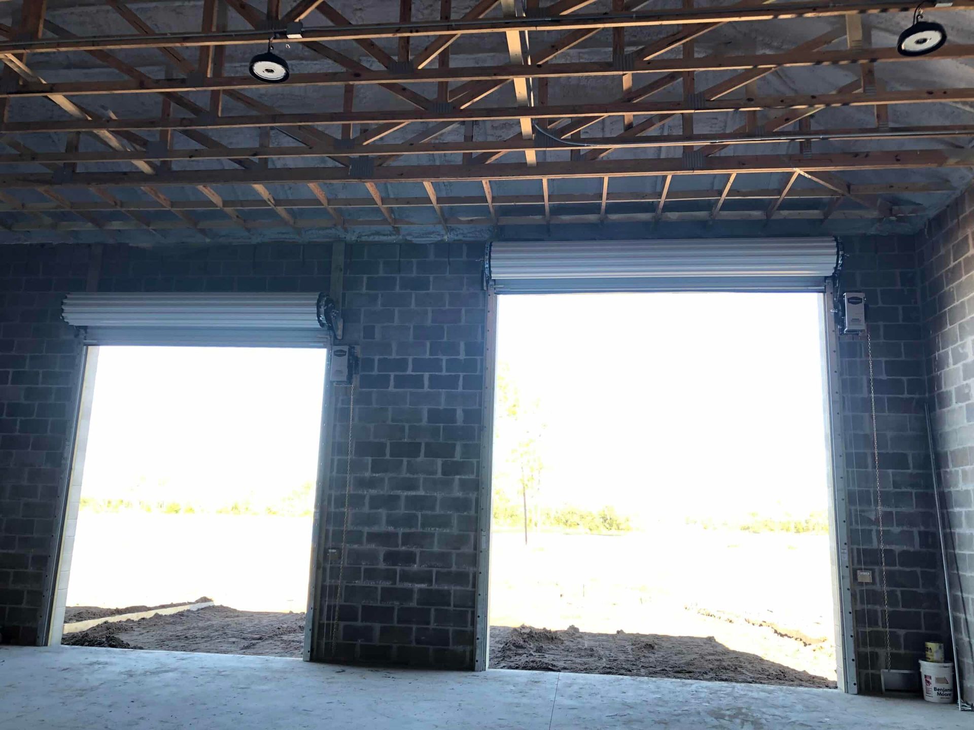 Interior of a brick building under construction with two large open garage-style doorways and exposed ceiling beams
