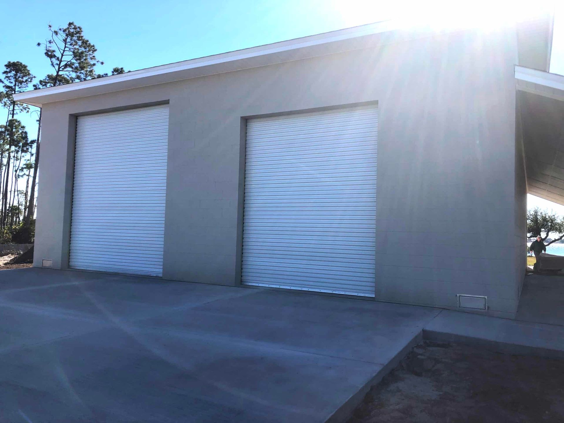 Small gray industrial building with two white roll-up garage doors in bright sunlight.
