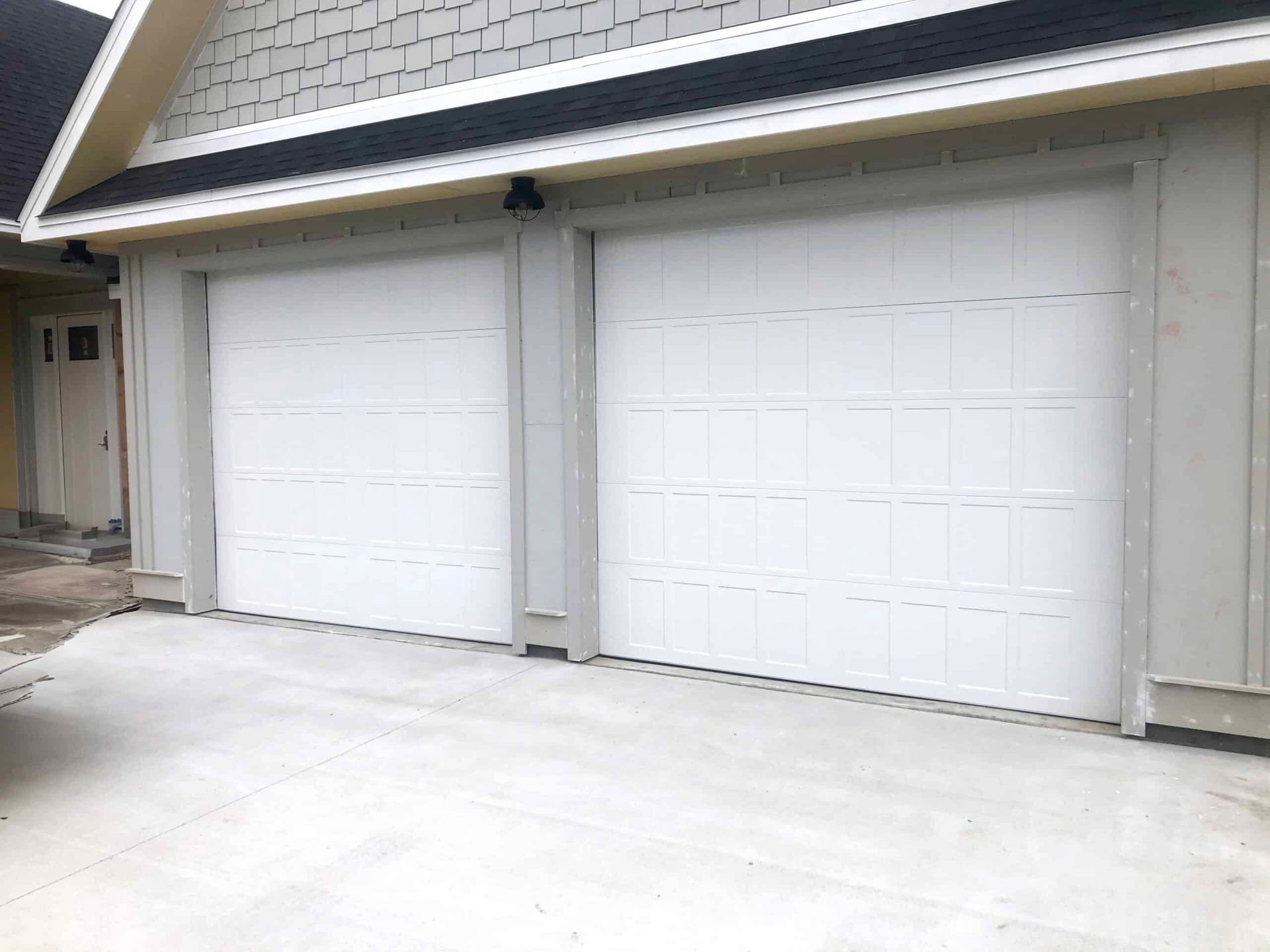 Two white garage doors on a light gray house exterior with a concrete driveway