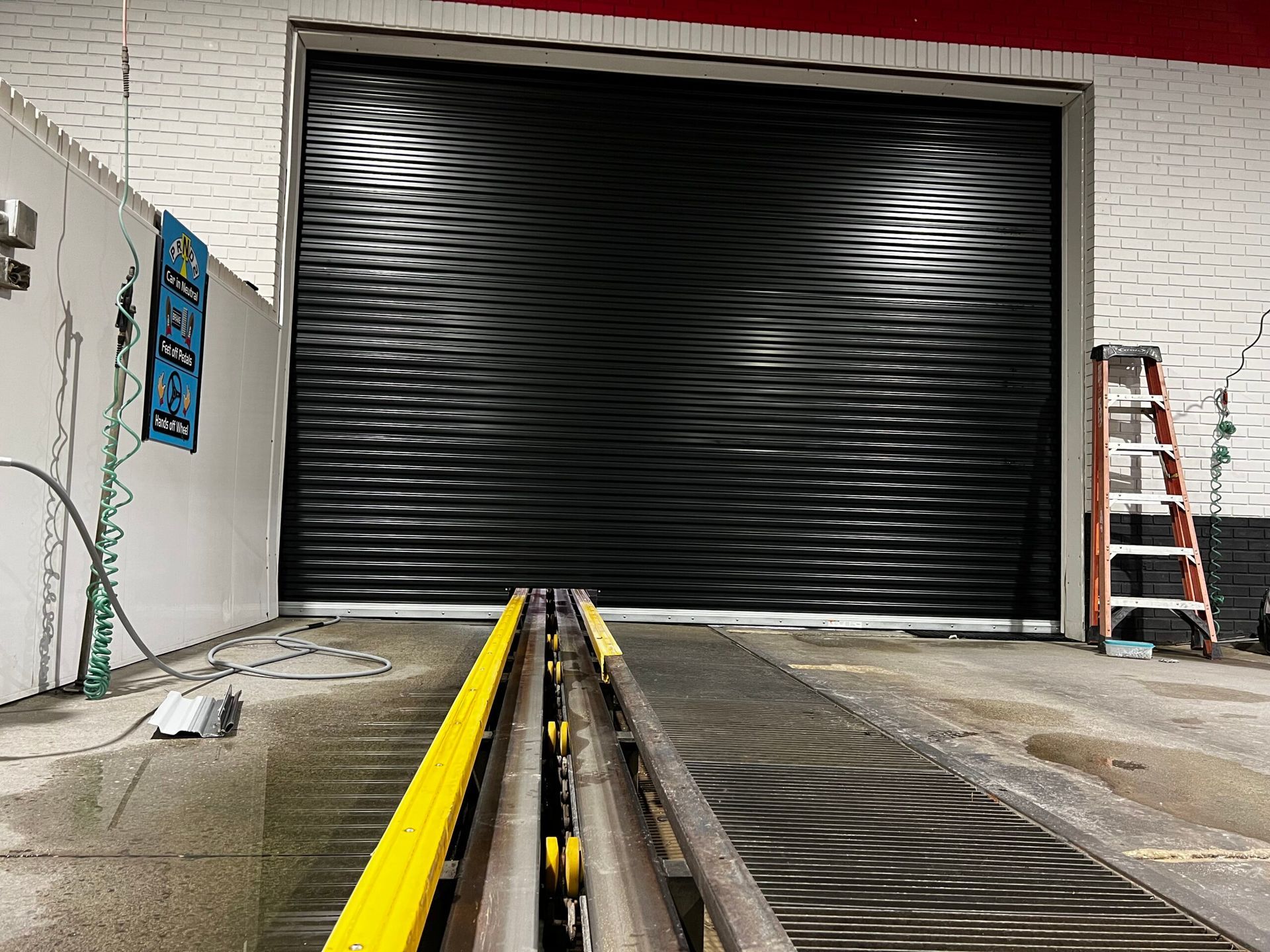 Industrial doorway with a large black roll-up door, yellow floor rails, and a ladder in a warehouse hallway