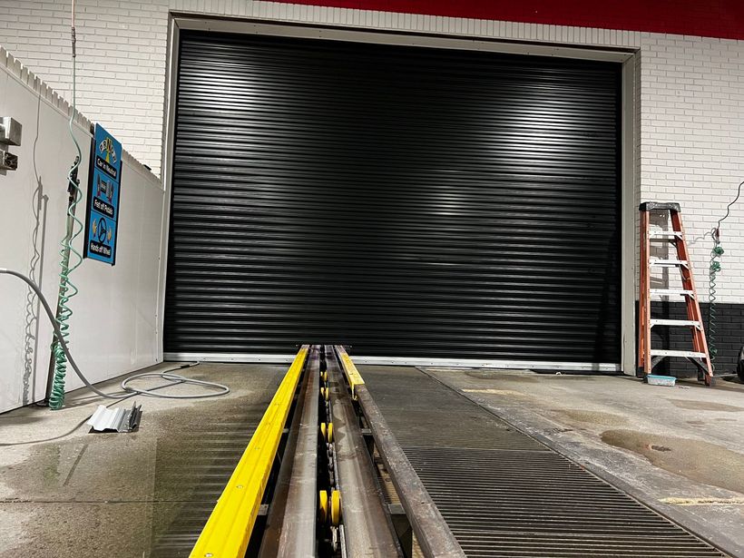 Closed gray industrial roll-up door with windows, inside a warehouse.