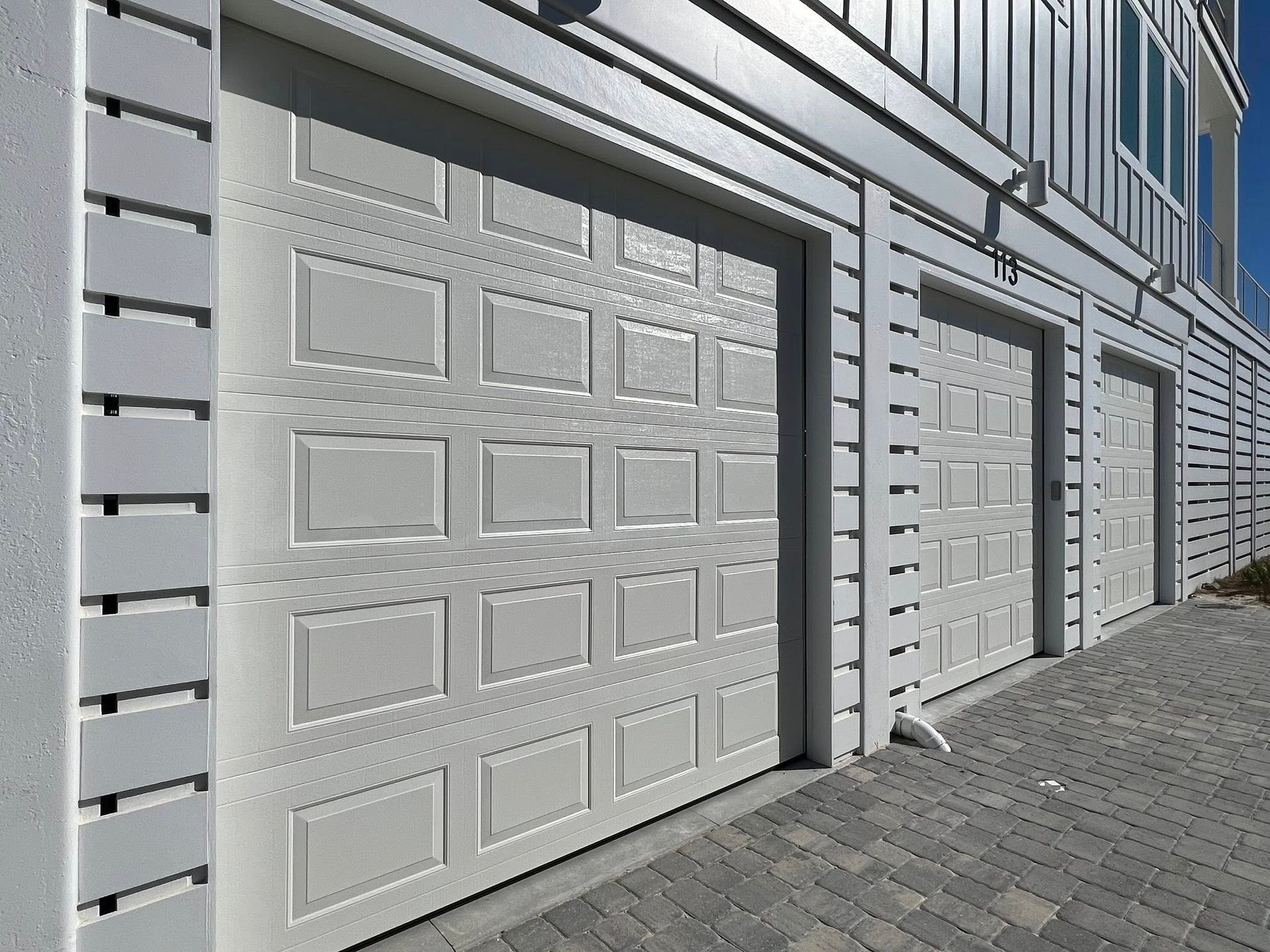 Row of white garage doors on a modern building with gray siding and a paved walkway