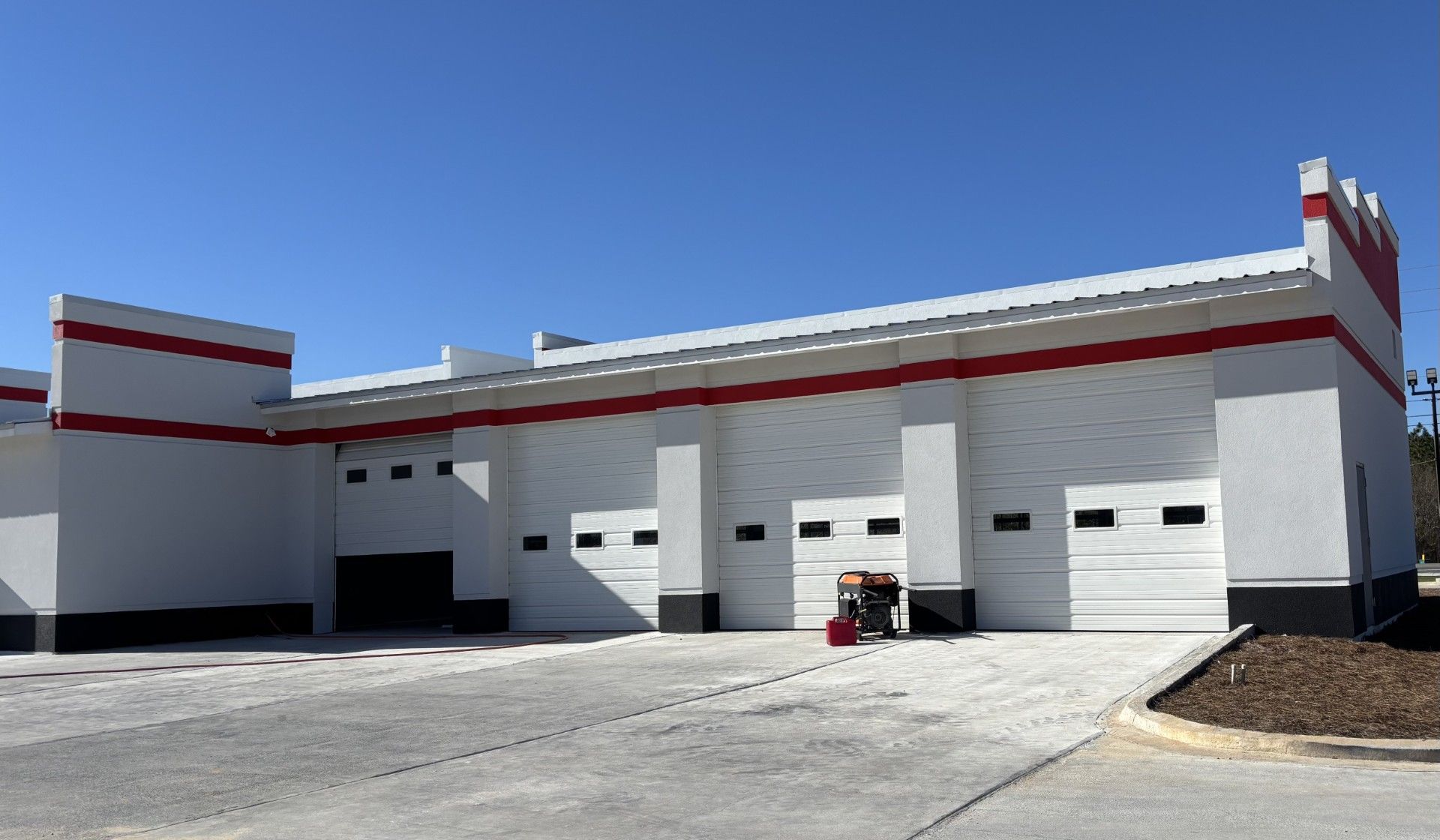 White commercial building with red trim and garage doors under a clear blue sky