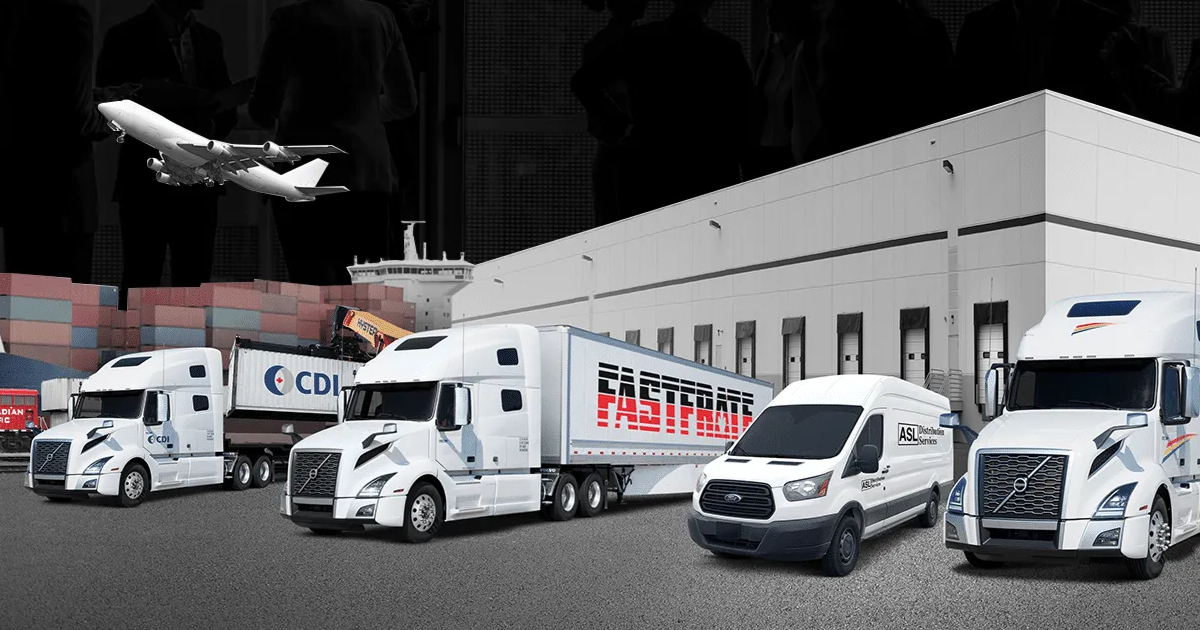 Four white delivery trucks and vans parked in front of a warehouse at night, with a plane overhead