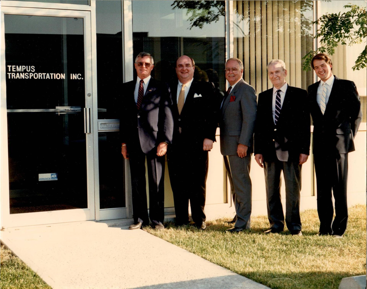 Five men in suits stand outside Tempus Transportation, Inc. office entrance.