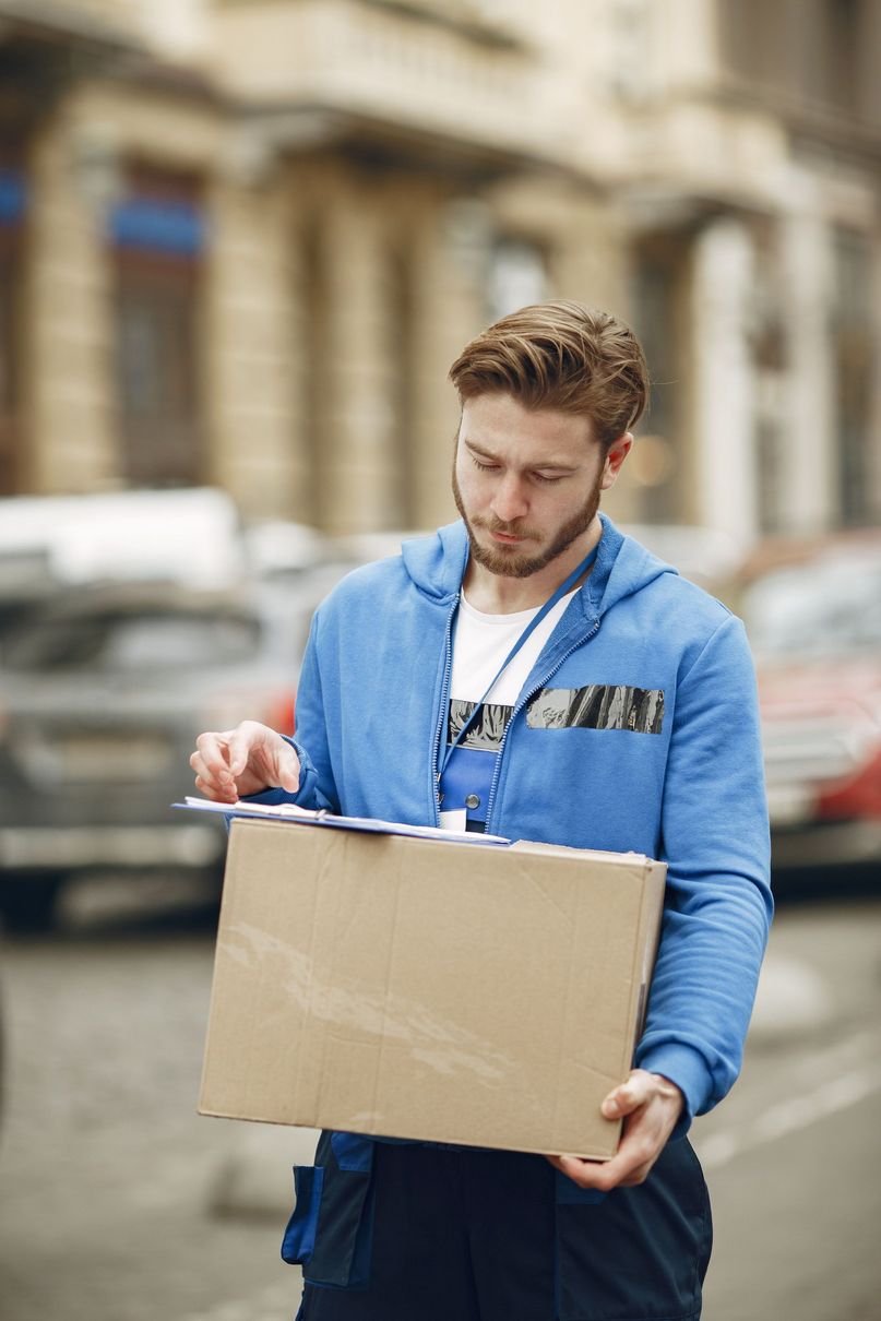 Man in blue jacket holding and examining a cardboard package on a city street