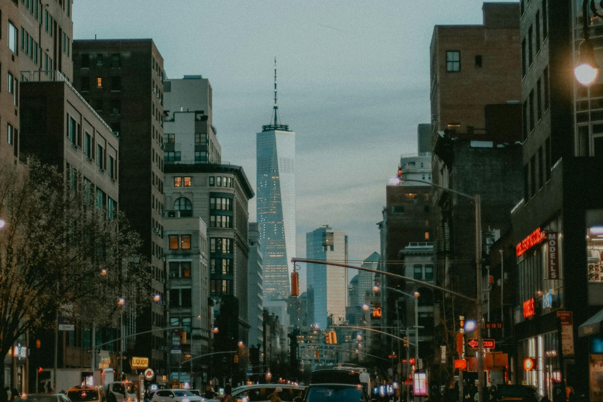 City street scene with skyscrapers, dusk sky, and glowing lights.