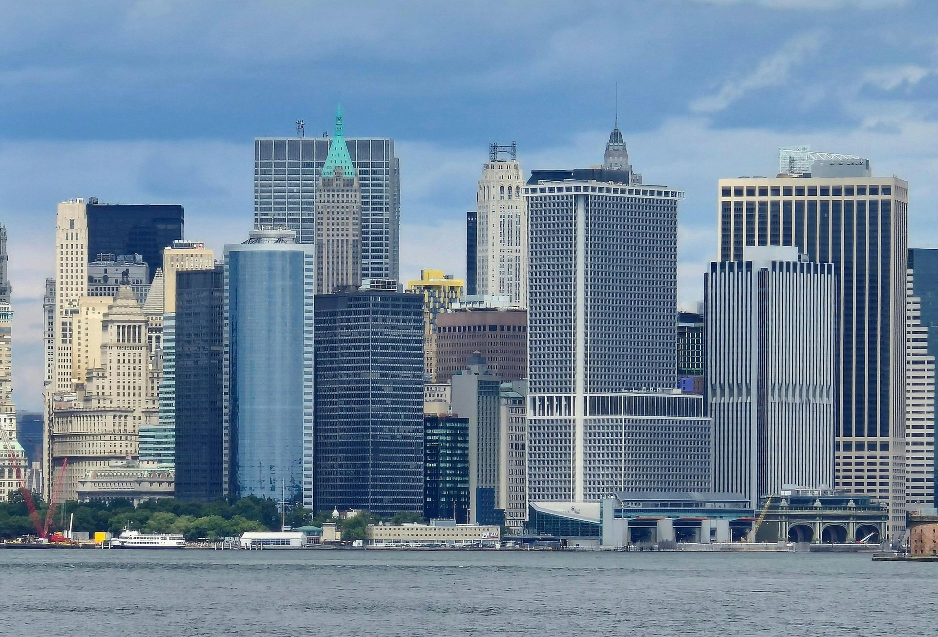 New York City skyline with many skyscrapers under a cloudy sky, seen from across the water.