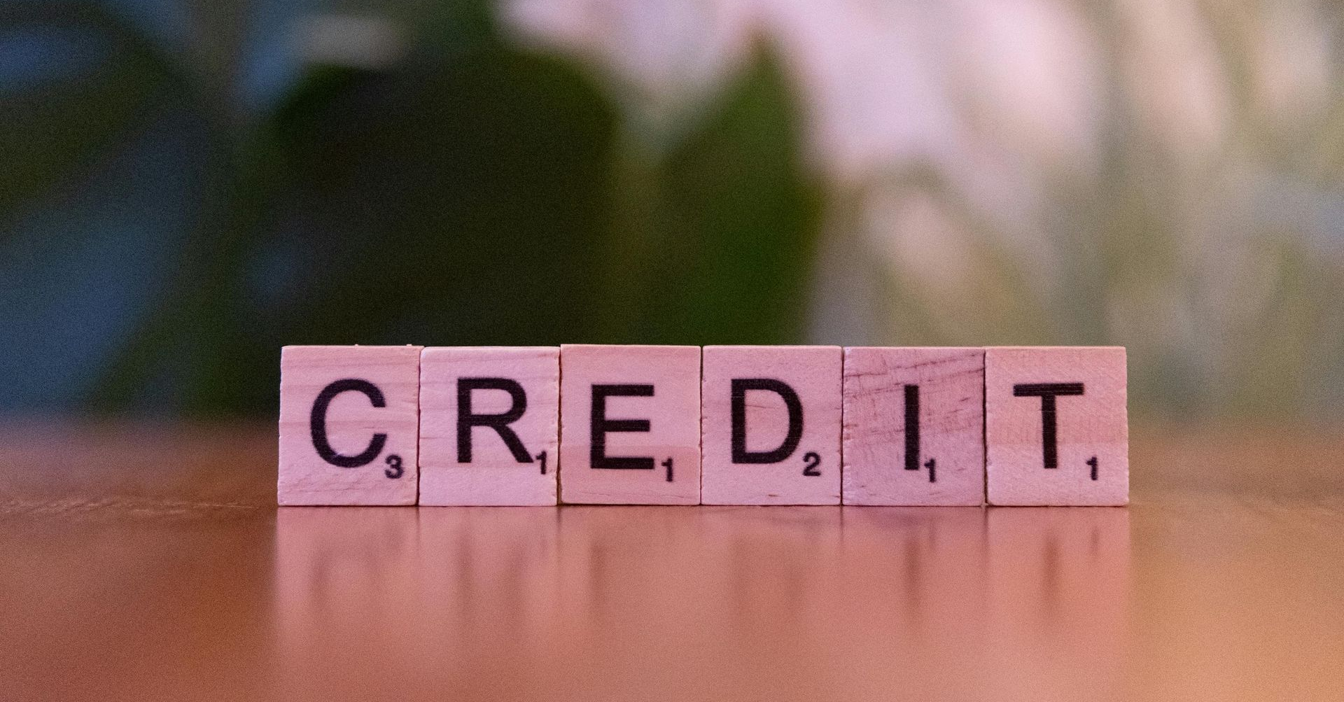 Wooden tiles spelling “CREDIT” on a reflective surface with a blurred background.