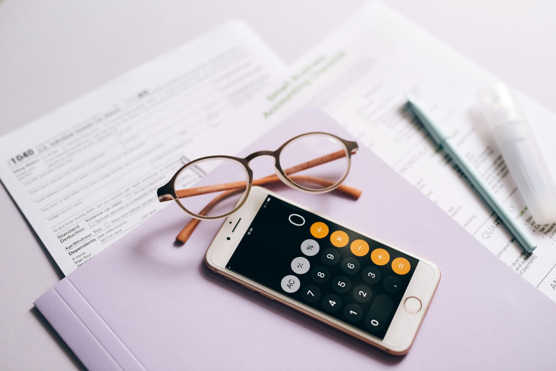 Smartphone calculator, glasses, pen, documents, and a purple folder on a light surface.
