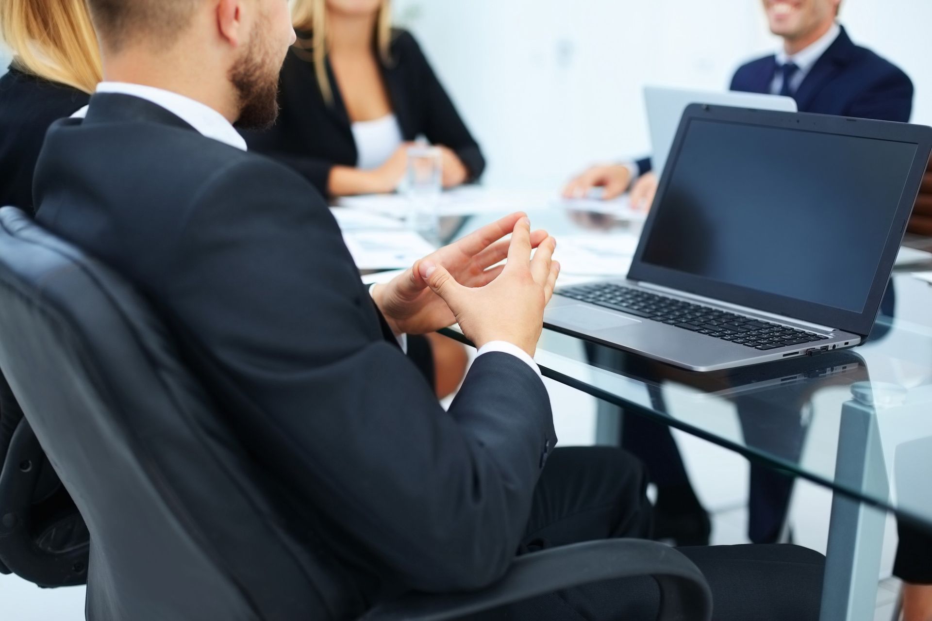 Business meeting with people seated at a glass table and an open laptop in the foreground