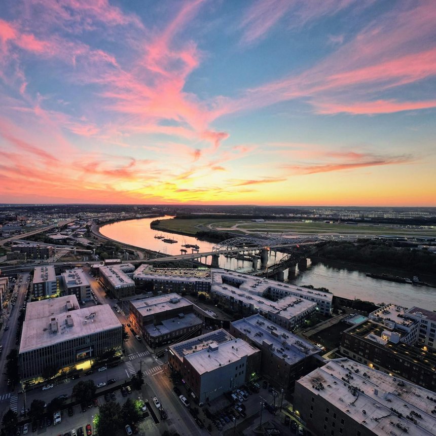 Aerial view of a city at sunset with a winding river and pink-orange sky
